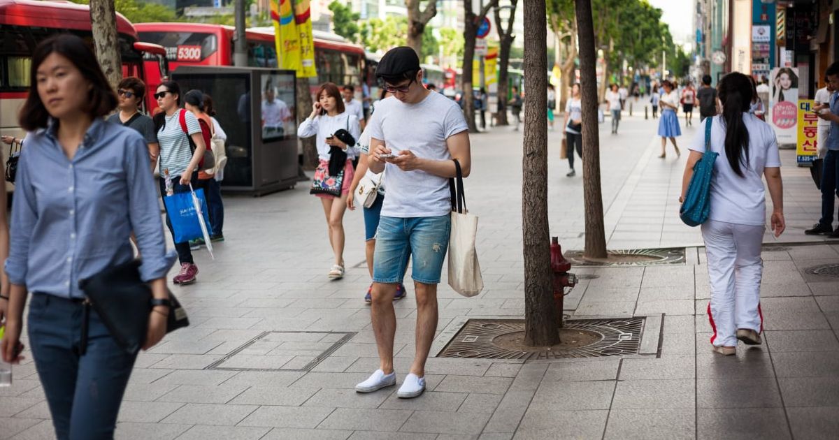 A person using a smartphone in Seoul with the city's neon-lit skyline in the background, representing Korea's mobile-first digital culture.